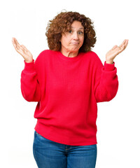 Beautiful middle ager senior woman red winter sweater over isolated background clueless and confused expression with arms and hands raised. Doubt concept.