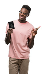 Young african american man holding canadian passport very happy pointing with hand and finger to the side