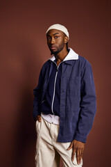 Handsome African American man standing confidently in front of a brown wall.