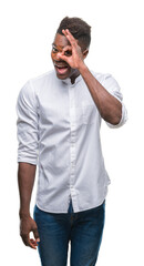 Young african american man over isolated background doing ok gesture with hand smiling, eye looking through fingers with happy face.