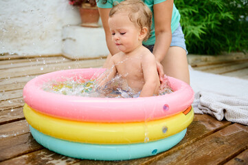 Happy baby splashing in inflatable pool with parent on sunny day