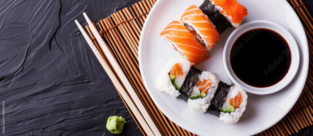 Aufkleber Top view of a round white plate with sushi chopsticks ginger and soy sauce on a dark bamboo mat background with ample copy space for an image