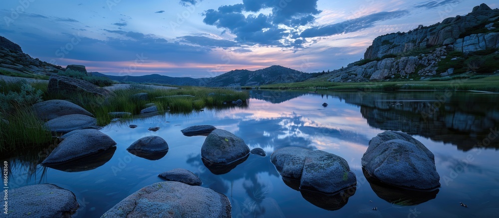 Poster Tranquil nature scene with rocks in the foreground mirrored in a lake under a twilight sky providing a serene ambience for a copy space image
