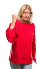 Middle age blonde woman over isolated background angry and mad raising fist frustrated and furious while shouting with anger. Rage and aggressive concept.