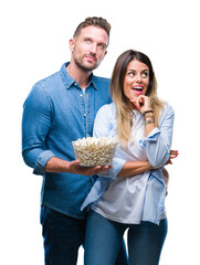 Young couple in love eating popcorn over isolated background serious face thinking about question,...