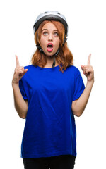 Young beautiful woman wearing cyclist helmet over isolated background amazed and surprised looking up and pointing with fingers and raised arms.