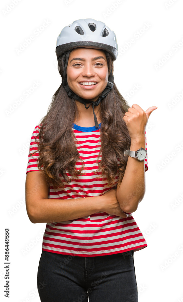 Wall mural Young arab cyclist woman wearing safety helmet over isolated background smiling with happy face looking and pointing to the side with thumb up.