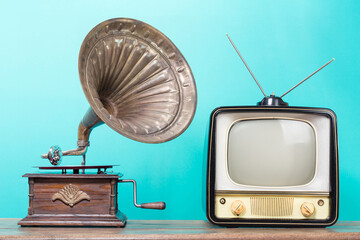 Retro TV and antique gramophone phonograph turntable with brass horn on old wooden table front mint blue background. Vintage style filtered photo