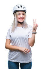 Young blonde woman wearing cyclist security helmet over isolated background smiling with happy face winking at the camera doing victory sign. Number two.
