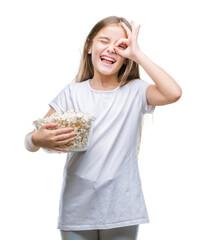 Young beautiful girl eating popcorn snack isolated background with happy face smiling doing ok sign with hand on eye looking through fingers