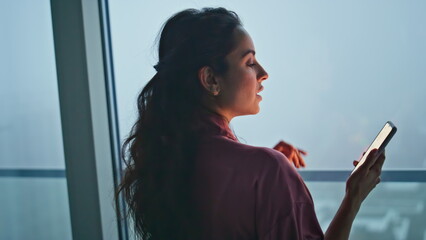 Brunette woman calling mobile phone at panoramic evening window flat back view