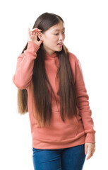Fototapeta premium Young Chinese woman over isolated background wearing sport sweathshirt smiling with hand over ear listening an hearing to rumor or gossip. Deafness concept.