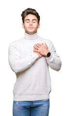 Young handsome man wearing turtleneck sweater over isolated background smiling with hands on chest with closed eyes and grateful gesture on face. Health concept.