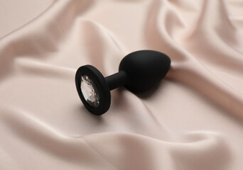 Black anal plug on beige silky fabric. Sex toy