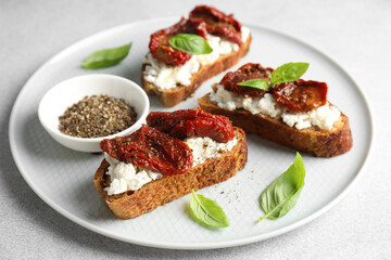 Delicious ricotta bruschettas with sun dried tomatoes, basil and milled pepper on light table, closeup