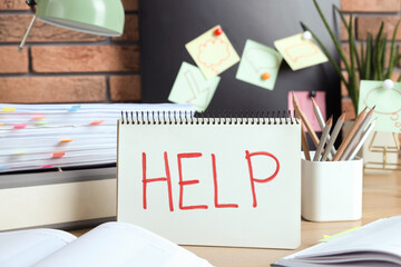 Notebook with word Help and stationery on wooden table at workplace