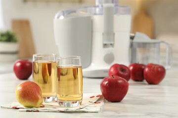 Glasses of fresh juice, pears, apples and modern juicer on white marble table in kitchen, selective focus
