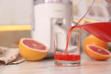 Pouring tasty grapefruit juice into glass at white marble table in kitchen, closeup