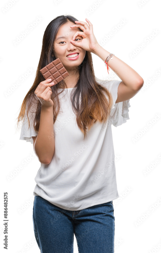 Canvas Prints Young asian woman eating chocolate bar over isolated background with happy face smiling doing ok sign with hand on eye looking through fingers