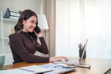 Young beautiful woman talking on mobile phone and using laptop sitting at her working place