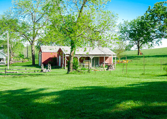 Red barn farmhouse on large acre lot farmland in Mansfield Missouri, grassy lawn and lush greenery trees, scenic peaceful agriculture town at agro-town agglomeration rural environment farmstead © trongnguyen