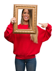 Beautiful young woman holding vintage frame very happy pointing with hand and finger