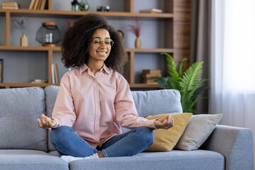 Woman sitting cross-legged on sofa meditating with a smile. Creating a relaxing and peaceful atmosphere in a cozy living room setting with natural light and houseplants.