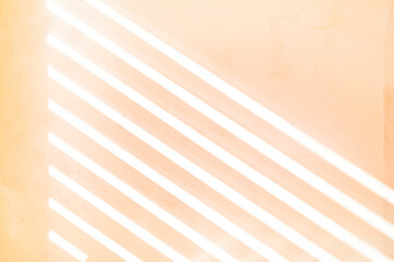 Sunlight through a slatted window blind onto a textured painted wall, peach fuzz color background,...