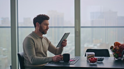Blurred man reading tablet sitting panoramic kitchen table at morning closeup