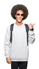 Young african american man with afro hair wearing sunglasses and backpack pointing and showing with thumb up to the side with happy face smiling