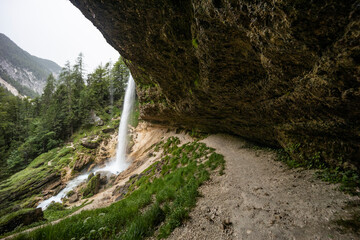 Obraz premium Perichnik waterfall is a beautiful drop from the mountain cliff, in Triglav National Park. Slovenian waterfall. Long for walking and trekking, enter inside the cave to admire it. Power and majesty.