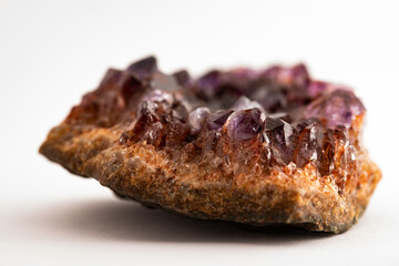 vista macro di un pezzo di una pietra minerale, stratificata e con tanti cristalli dalle sfumature di color viola, in primo piano, con sfondo bianco