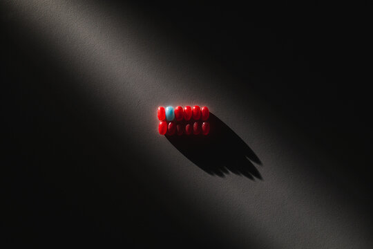 concetto di unico tra i tanti, essere diversi, essere quello diverso nel gruppo. file di caramelle rosse di cui soltanto una &egrave; azzurra, illuminate da un fascio di luce