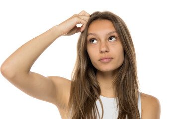 Fototapeta premium Portrait of a young teenage girl thinking and scratching her head with her finger on a white studio backgroun
