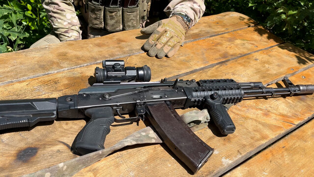 An Ak-74 Kalashnikov assault rifle with an optical sight lies on the table in front of the fighter. Close-up. Armament of the army during the war. A real war.