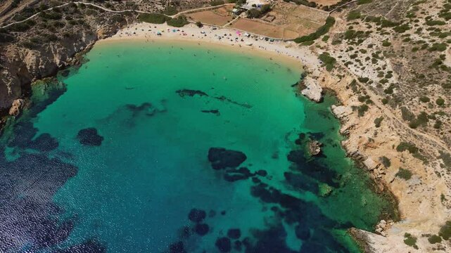 Overlooking a private beach on Donousa Island, Greece with turquoise waters, rocky formations, and sunbathers on the sandy shore