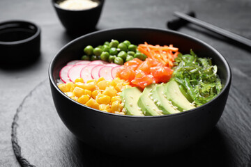 Delicious salad with salmon, vegetables and seaweed on black table, closeup