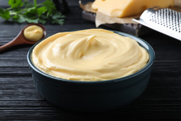 Tasty cheese sauce in bowl on black wooden table, closeup