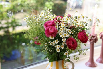 Beautiful ranunculus flowers and chamomiles in vase on windowsill indoors
