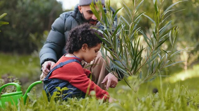 A caring dad teaches his young son to plant a tree, symbolizing growth and bonding in nature.