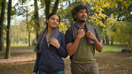 Fototapeta premium Indian man with Arabian woman friends wife husband girl guy boyfriend girlfriend walking together after running workout sport training outdoors in forest park nature talking friendly communicating
