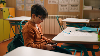 School education studying Caucasian boy little son schoolboy kid child pupil student schoolboy at class lesson gadget addict mobile phone addiction playing online video game hide smartphone under desk