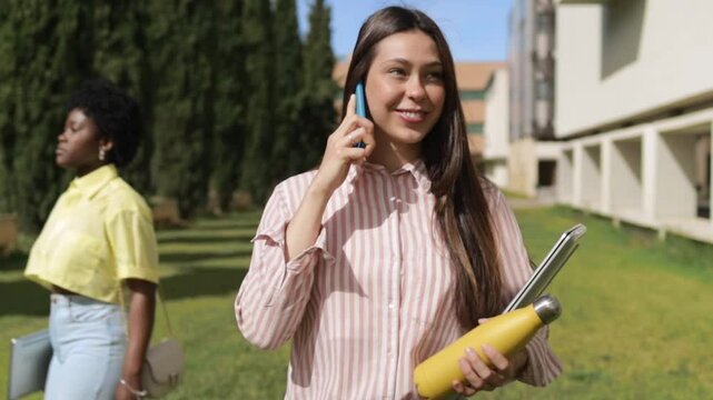 Pretty student talking on smartphone and walking in college campus.