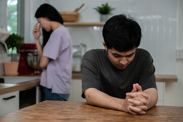Obraz premium Young couple relation problem concept : Young Asian man feeling sad and crying after have an argument at home. Sad or depressed guy sitting at table with her couple. Couple relation conflict concept.