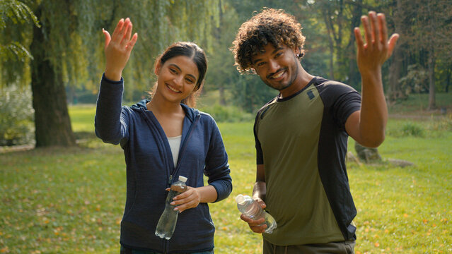 Two sport people smiling talking holding water bottles smile invitation join to exercise male Indian female Arabian friends couple man woman in park invite welcome workout fitness fit in city motivate