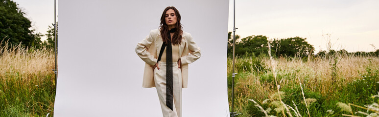Obraz premium A beautiful young woman in white attire stands gracefully in a field of tall grass, embracing the gentle summer breeze.