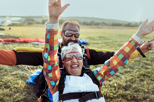 Smiling senior woman landing with skydiving instructor on field
