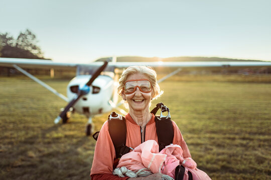 Portrait of a happy smiling senior woman on field after skydiving at sunset