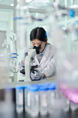 Young brunette woman in lab coat and protective gloves studying new chemical substance in...