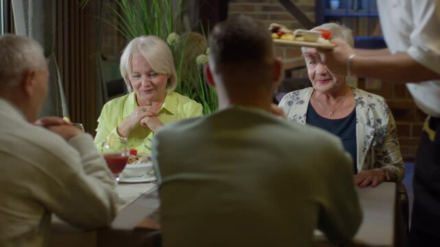 Waiter Serving Food for Two Senior Women Sitting at the Restaurant Table with Two Men. Concept of Family Time, Fine Dining, Customer Service, Eating Out, Dinner
